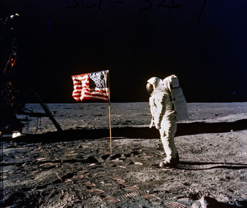 Photograph of Buzz Aldrin in space suit on the moon. US Flag is planted in the ground.