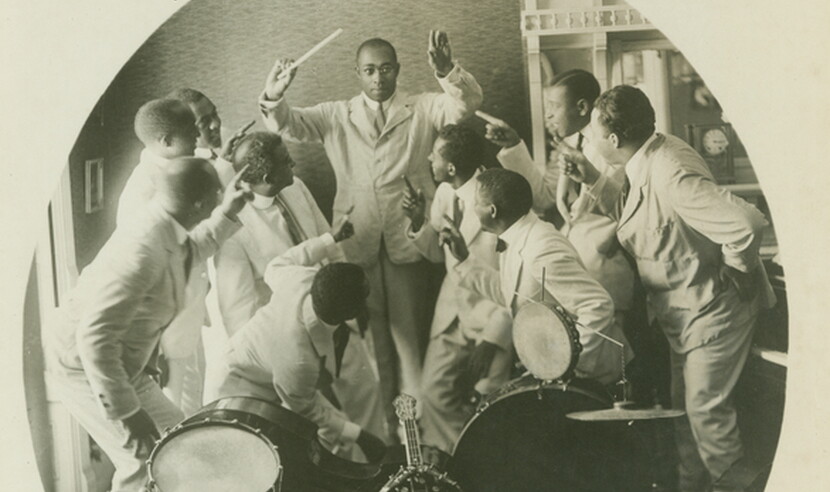 Photograph of James Reese with his band. He is shown conducting as the band members point at him.