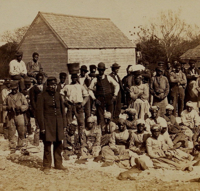 Lives of the Enslaved (Civil War era photo of a large group of enslaved people gathered outside. Women are sitting on the ground while the men stand behind them.)