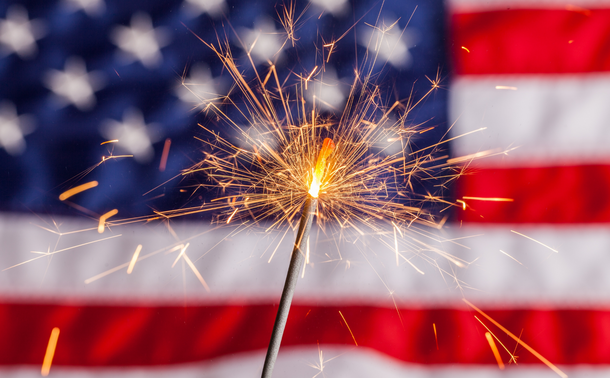 A sparkler burns with an American flag in the background