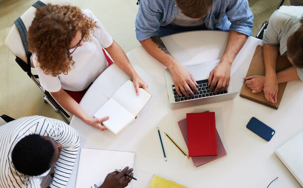 A group of teens in casual wear sitting around table carrying out homework.