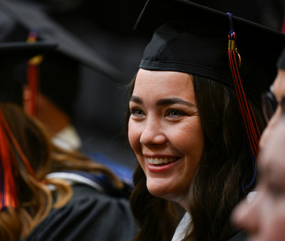 View of two graduating MA program students in cap and gown (one in the foreground, the other in the background) at the inaugural Gettysburg Commencement Ceremony