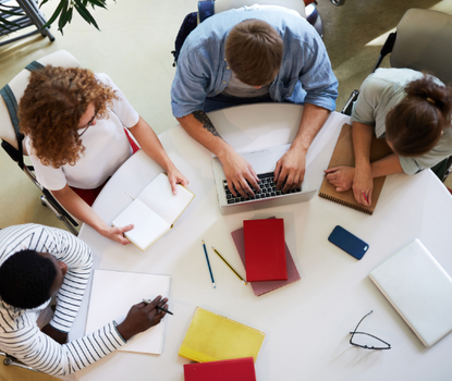 View from above showing four students gathered around a round table with notepads and laptops