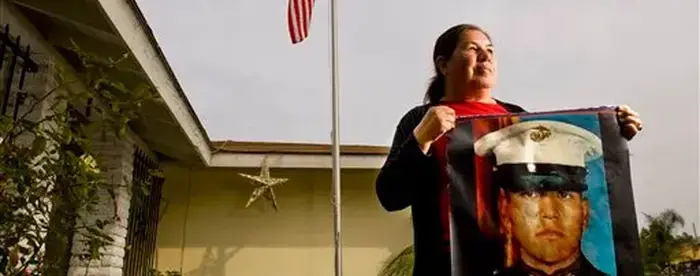 Photograph of Simona Garibay holding a banner of her son in front of US flag