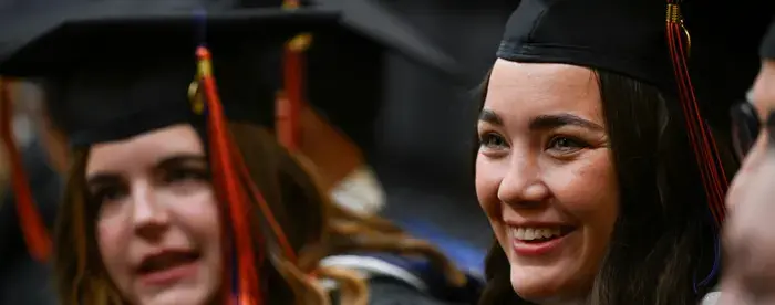 View of two graduating MA program students in cap and gown (one in the foreground, the other in the background) at the inaugural Gettysburg Commencement Ceremony