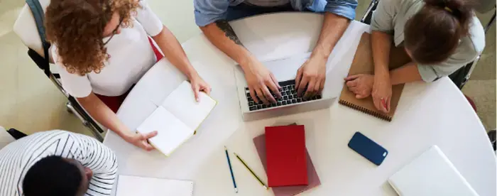 View from above showing four students gathered around a round table with notepads and laptops