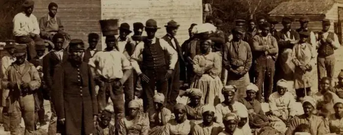 Group of emancipated enslaved people sitting in yard. With buildings visible in background.