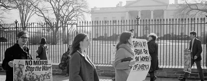 A photograph of anti-Vietnam War demonstrators carrying signs, "No more...Stop the war!", "Eartha Kitt speaks for the women of America", and "Stop the draft", picketing in front of the White House.