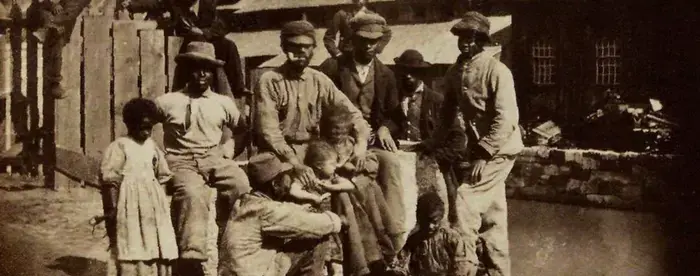 Group of 12 negro adults and children in front of a partially destroyed building