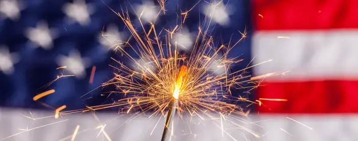 A sparkler burns with an American flag in the background