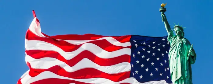 Statue of Liberty with US Flag waving in background against blue sky