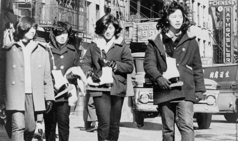 A black and white photograph of four Chinese American young women carrying ice skates in Chinatown.