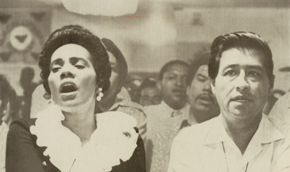 Photograph of Coretta Scott King and Cesar Chavez holding heads during a religious service