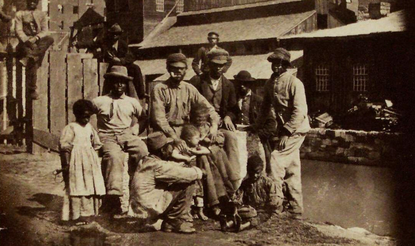 Group of 12 negro adults and children in front of a partially destroyed building