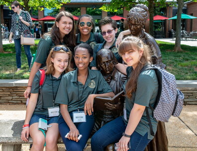 A group of seven students from the National History Academy in green uniforms posed around a bronze statue