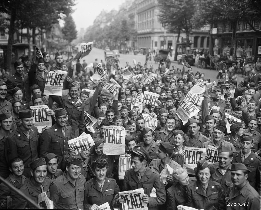 Crowd of military Service members holding up newspapers with "PEACE" headline in large letters